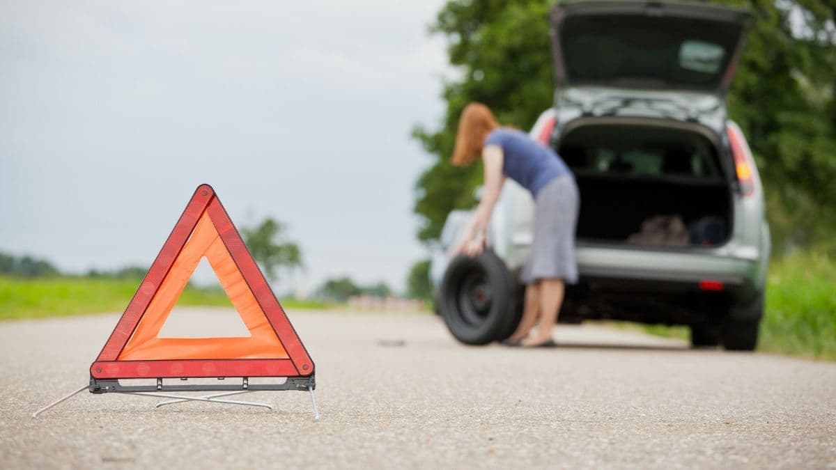 mulher sinalizando o local para começar a trocar o pneu do carro que furou